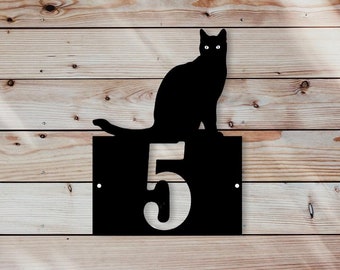 May include: Black metal house number sign with a silhouette of a cat sitting on top of the number "5".