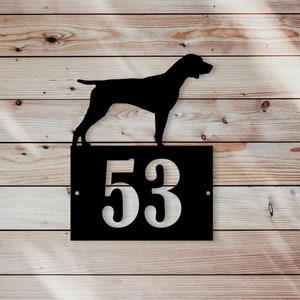 Op de afbeelding: Zwart metalen huisnummerbord met het nummer 53 uitgesneden. Een silhouet van een hond staat bovenop het bord.