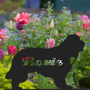 Può includere: Silhouette di cane in metallo nero con il nome "Rosie" tagliato dalla silhouette. La silhouette è in piedi in un giardino con fiori rosa e viola.