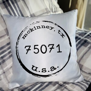 May include: White cushion with a black and white circular design that says "mckinney, tx 75071 u.s.a."