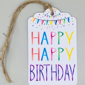 May include: A white gift tag with a colourful happy birthday message. The tag has a rainbow design with confetti and a string of flags. The tag is tied with a brown twine string.