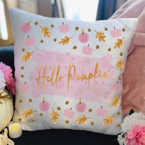 May include: White throw pillow with a pink watercolor background and gold lettering that says "Hello Pumpkin". The pillow is decorated with pink pumpkins and gold leaves.