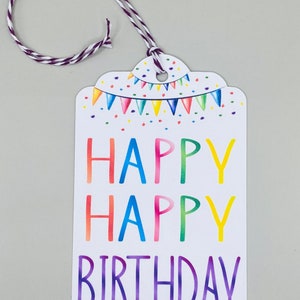 May include: A white gift tag with a colourful rainbow design. The tag has a string attached and says "Happy Happy Birthday" in a rainbow font.