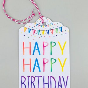 May include: A white gift tag with a colourful happy birthday message. The tag has a string attached to the top and is decorated with a rainbow-coloured bunting.