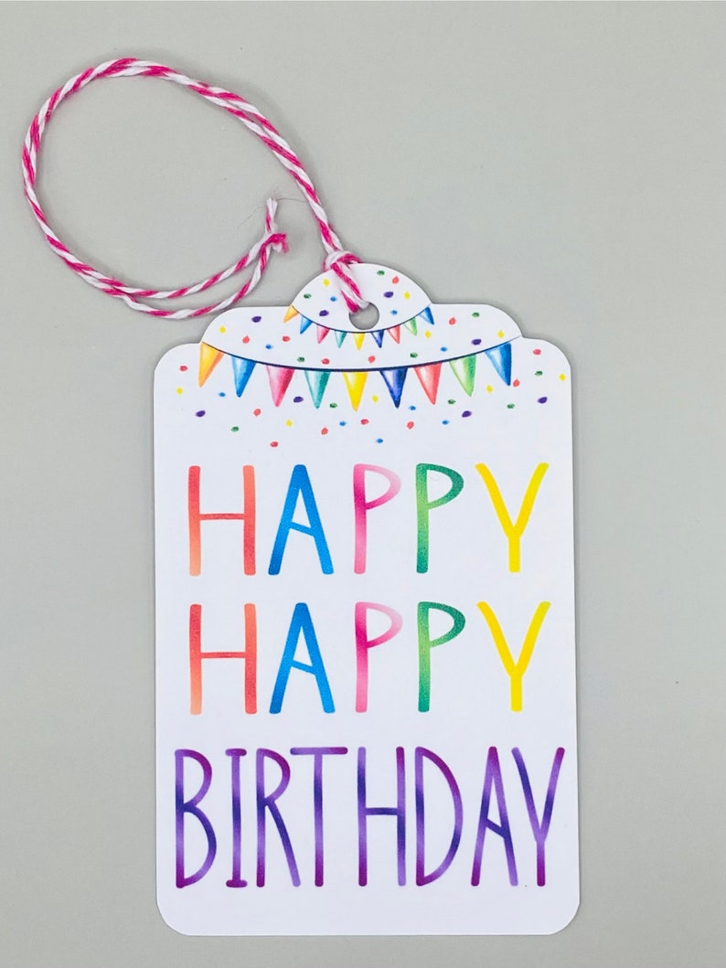 May include: A white gift tag with a colourful happy birthday message. The tag has a string attached to the top and is decorated with a rainbow-coloured bunting.