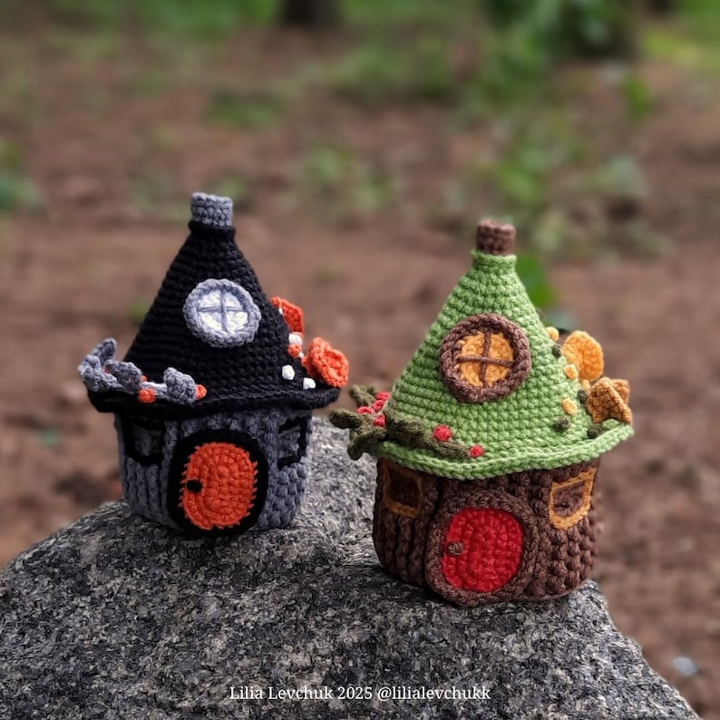 May include: Two crocheted fairy houses. One is black and gray with an orange door and accents. The other is brown and green with a red door and decorative elements. Both have conical roofs and round windows.