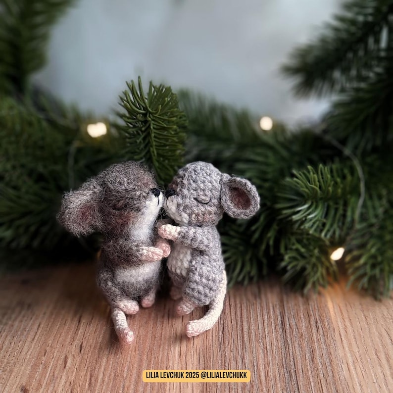 May include: Two crocheted gray mice are embracing, their eyes closed. One mouse has a darker gray body and the other is a lighter gray. The mice are on a wooden surface with a blurred green background. Text at the bottom reads "LILIA LEVCHUK 2025 @LILIALEVCHUKK."