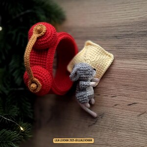 May include: A handmade crochet scene featuring a red headset with a tan cord, a gray mouse, and a yellow pillow. The mouse is curled up next to the pillow. The scene is set on a wooden surface. Text in the image reads: LILIA LEVCHUK 2025 @LILIALEVCHUKK.