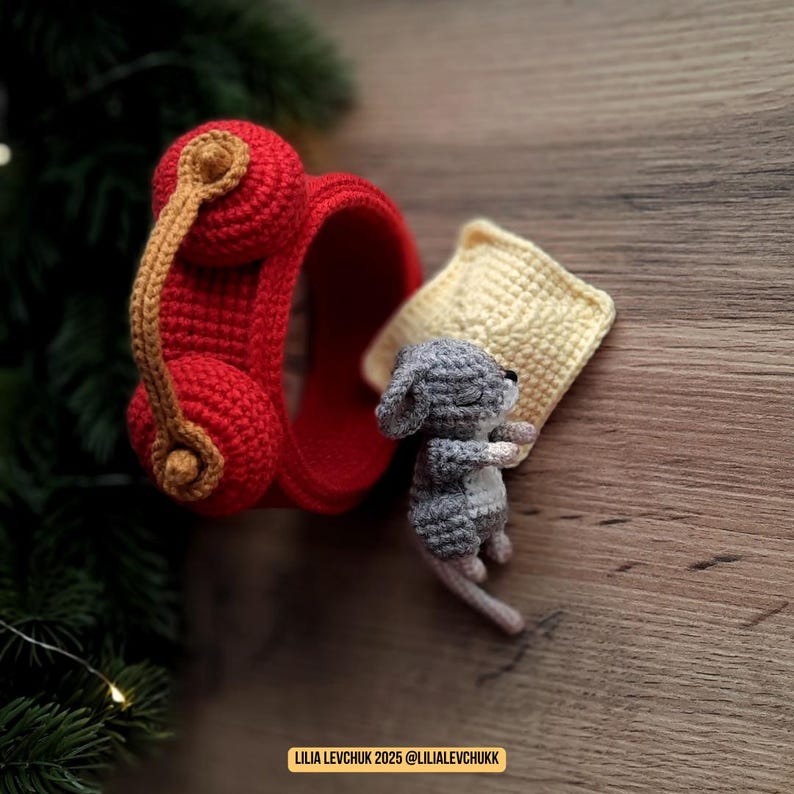 May include: A handmade crochet scene featuring a red headset with a tan cord, a gray mouse, and a yellow pillow. The mouse is curled up next to the pillow. The scene is set on a wooden surface. Text in the image reads: LILIA LEVCHUK 2025 @LILIALEVCHUKK.
