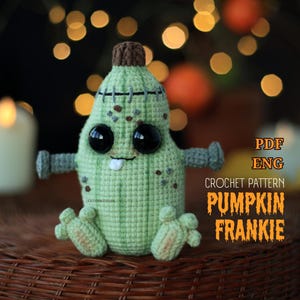 May include: A light green crocheted pumpkin figure with a brown stem, large black eyes, a single white tooth, and grey arms. The text on the right reads PDF ENG CROCHET PATTERN PUMPKIN FRANKIE. The figure has stitched details and a textured surface.