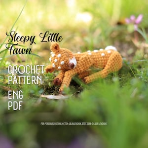 Könnte beinhalten: Ein gehäkeltes Reh in Braun- und Weißtönen, das auf grünem Gras liegt. Das Reh hat weiße Flecken und ist mit "Sleepy Little Fawn" beschriftet. Das Bild enthält auch den Text "CROCHET PATTERN ENG PDF".