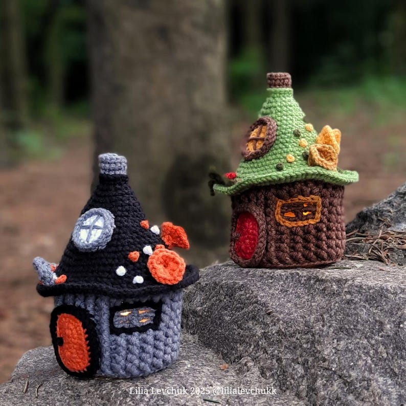 May include: Two crocheted fairy houses. One is gray and black with orange accents, the other is brown and green. Both have small windows and doors. The houses are sitting on a rock. The text "Lilia Levchuk 2025 @lilialevchuk" is at the bottom.