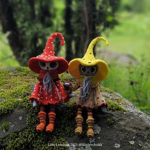 May include: Two handmade crochet dolls, one in red with white polka dots and the other in yellow, are holding hands. They wear matching hats and dresses, with gray scarves and boots. The dolls are set against a blurred green background.