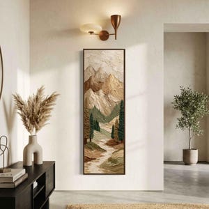 May include: Vertical framed landscape art depicting a mountain scene with textured brushstrokes. The artwork shows a river winding through a valley, with green trees and beige and brown mountains. The frame is dark brown.