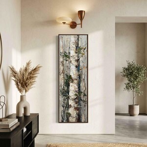 May include: Vertical framed artwork featuring a textured painting of birch tree trunks. The painting uses shades of white, gray, and brown, with green accents. The artwork is displayed on a light-colored wall, with a modern light fixture above.