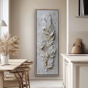Peut inclure: Une œuvre d'art murale verticale encadrée, avec un fond texturé blanc cassé et des motifs de plumes blanches en trois dimensions. L'œuvre est encadrée dans un cadre fin de couleur or, adaptée à la décoration intérieure.