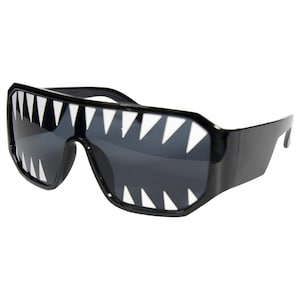 May include: Black sunglasses with a bold, rectangular frame. The lenses are dark, and the top of the frame features a row of white, triangular teeth-like shapes, creating a unique and edgy design.
