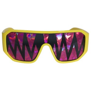 K&ouml;nnte beinhalten: Gelb gerahmte Sonnenbrille mit einem auff&auml;lligen geometrischen Design auf den Gl&auml;sern. Die Gl&auml;ser zeigen ein lebendiges, irisierendes Muster in Rosa- und Lilat&ouml;nen, kontrastiert von schwarzen Zickzackformen. Ein einzigartiges Brillenaccessoire.