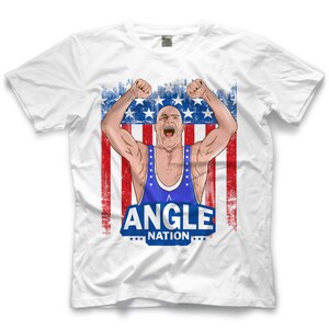 Puede incluir: Camiseta blanca con un gráfico de un luchador en un maillot azul con el texto "Angle Nation" sobre un fondo de bandera estadounidense rojo, blanco y azul.