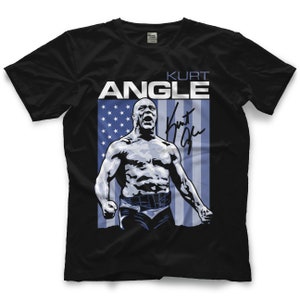 Puede incluir: Camiseta negra con un diseño de bandera americana azul y blanca. La bandera tiene la silueta de un luchador delante de ella. El texto "KURT ANGLE" está por encima de la bandera y la firma del luchador está a la derecha de la bandera.