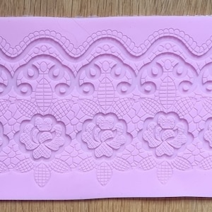 Puede incluir: Un molde de silicona morado con un diseño en relieve de un borde de encaje con acentos florales. El molde está diseñado para hornear y decorar pasteles y otros postres.