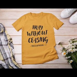 Puede incluir: Una camiseta amarilla mostaza con el texto "Pray Without Ceasing 1 Tesalonicenses 5:17" impreso en negro.