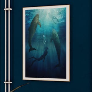 May include: A framed art print depicts a serene underwater scene with dolphins and a diver. The artwork features a palette of blues and greens, with sunlight filtering through the water. The print is displayed on a dark blue wall.
