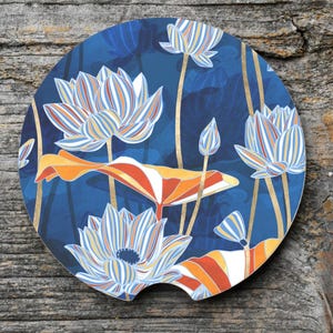 May include: A round car coaster featuring a blue background with a floral design. The design includes white, orange, and gold lotus flowers and leaves. The coaster has a small notch on one side.