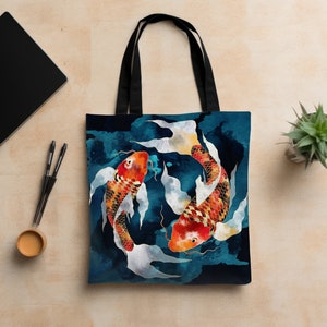 May include: A black tote bag with a design of two koi fish swimming in a circle against a blue and white watercolor background.