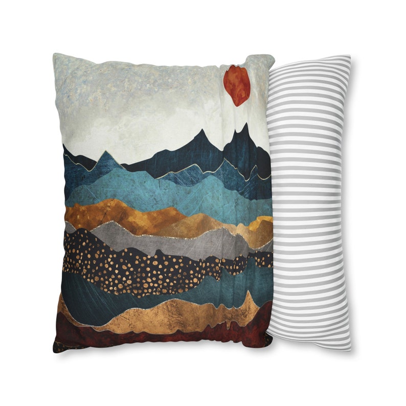 May include: Two decorative throw pillows. One pillow features a colorful abstract mountain landscape with a red sun in the top right corner. The other pillow is white with gray stripes.