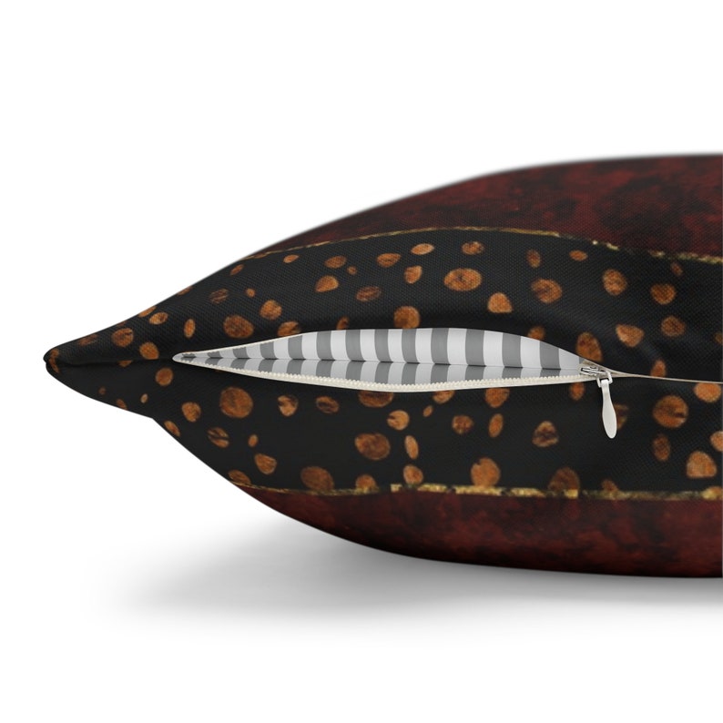 May include: A close-up of a pillow with a zipper closure. The pillow has a black background with a pattern of brown coffee beans and a red and gold stripe. The zipper is white with a black stripe.