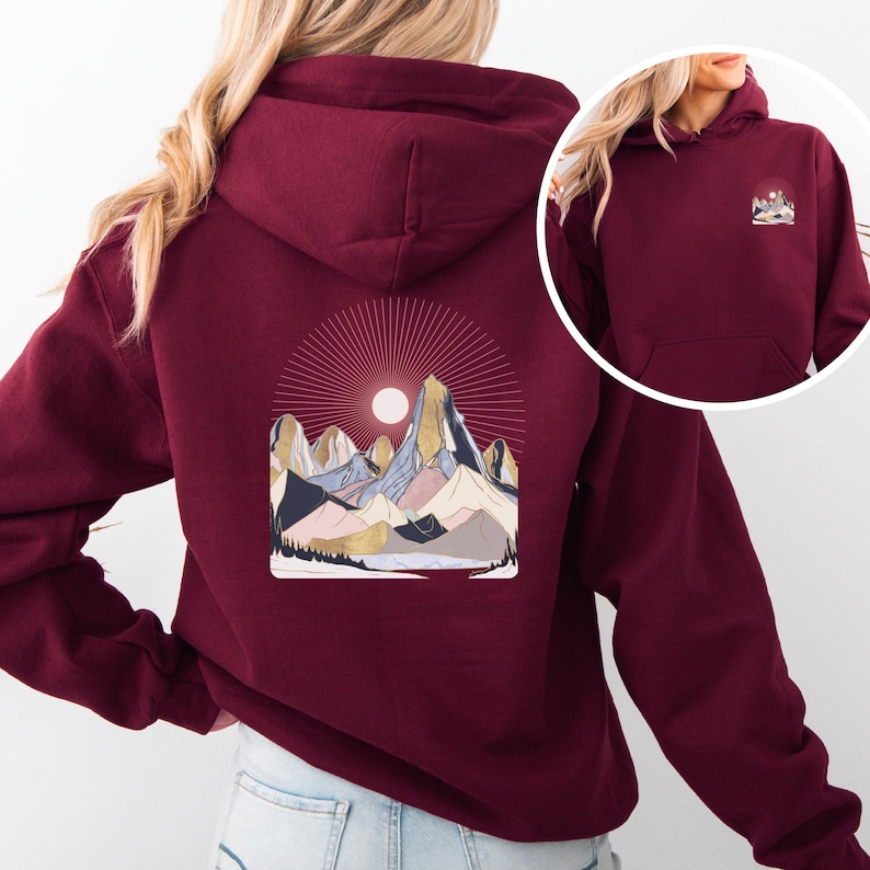 Pu&ograve; includere: Felpa con cappuccio bordeaux con grafica di catena montuosa sul retro e una versione pi&ugrave; piccola sul davanti. La grafica presenta un sole, montagne e un lago nei toni dell'oro, rosa, blu e nero. La felpa ha un cappuccio e una tasca frontale.