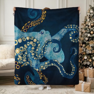 May include: A navy blue blanket featuring a watercolor octopus design. The octopus is depicted in shades of blue and gold, with intricate details on its tentacles. The blanket is held up, showcasing the full design.