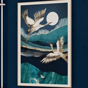 May include: A framed print of two white cranes flying against a blue and teal background with a full moon. The cranes are outlined in gold and the background has a watercolor effect.