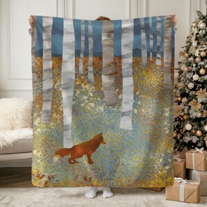 May include: A cozy blanket featuring an artistic forest scene with a red fox. The design includes tall, white birch trees with blue and gray accents, and a colorful, speckled ground. The blanket is held up, showcasing the full design.