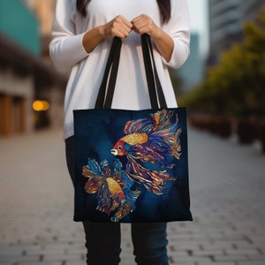 May include: A dark blue tote bag with a colorful illustration of two betta fish with flowing fins. The fish are outlined in gold and have red, orange, and purple accents.