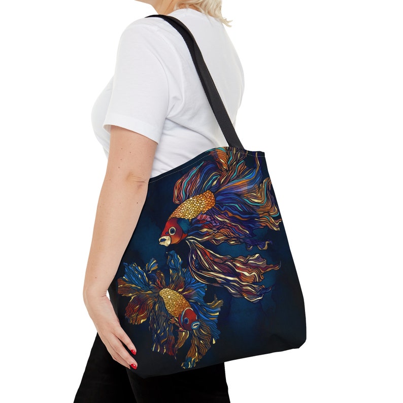 May include: A black tote bag with a colorful illustration of two betta fish on a dark blue background. The fish have red, orange, yellow, and blue fins.