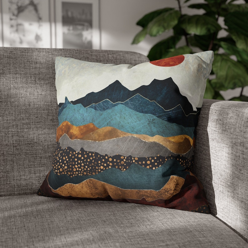 May include: A decorative throw pillow with a mountain landscape design. The pillow features a layered design with shades of blue, brown, gold, and red. The pillow is made of a soft, comfortable fabric and is perfect for adding a touch of style to any room.