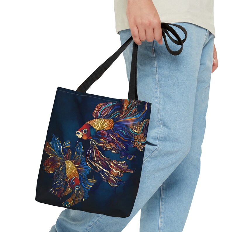 May include: A black tote bag with two colorful fish with gold accents on a dark blue background. The fish have flowing fins and tails.