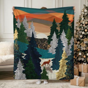 May include: A forest-themed blanket featuring a sunset scene with orange, teal, and gold hues. The design includes stylized evergreen trees, a fox, and a mountain range. The blanket is held up by a person.