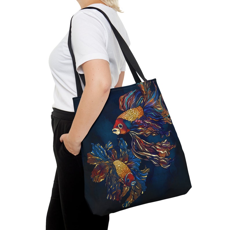 May include: A black tote bag with a colorful illustration of two betta fish on a dark blue background. The fish have red, orange, and yellow scales and flowing fins.