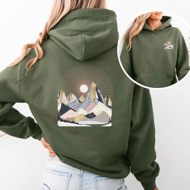 Pu&ograve; includere: Felpa con cappuccio verde oliva con grafica di catena montuosa sul retro e una grafica di montagna pi&ugrave; piccola sul davanti. La grafica della montagna presenta un sole, cime e vari colori tra cui blu, rosa e oro.