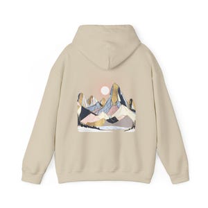 Pu&ograve; includere: Felpa con cappuccio beige con grafica di una catena montuosa sul retro. Il design include un sole, montagne nei toni del blu, rosa e oro e una silhouette di foresta. La felpa ha un cappuccio e maniche lunghe.