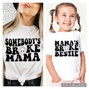 Könnte beinhalten: Zwei weiße T-Shirts mit schwarzem Text. Das größere Shirt sagt "Somebody's Broke Mama" mit einem Blitz in einem Kreis. Das kleinere Shirt sagt "Mama's Broke Bestie" mit einem Blitz in einem Kreis.