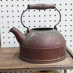 May include: A vintage copper tea kettle with a wooden handle. The kettle has a patina of age and is slightly tarnished.