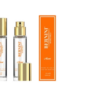May include: Two clear glass bottles of perfume with gold caps and labels that say "Bernini Beverly Hills Miami". The bottles are next to a rectangular orange box with the same label. The box says "Made in Italy Eau de Parfum 10 ml e 0.34 fl oz".