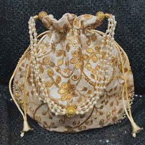 May include: Cream-coloured drawstring pouch with detailed gold embroidery of floral and leaf designs. The bag features a pearl beaded handle and a gold beaded tassel. The pouch is likely used for carrying small items.