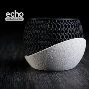 Op de afbeelding: Zwart-witte Echo orchideeënplanter met een uniek golfpatroon. De planter staat op een getextureerde, witte basis. De woorden "echo orchid planter" staan linksboven gedrukt.