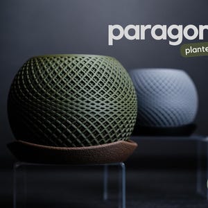 Könnte beinhalten: Zwei kugelförmige Pflanzgefäße mit Gittermuster. Eines ist olivgrün und steht auf einer braunen Untertasse, das andere ist hellgrau. Das Wort "paragon" steht über den Pflanzgefäßen, darunter "planter".