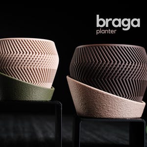Könnte beinhalten: Zwei dekorative Pflanzgefäße mit geometrischem Design. Eines ist hellrosa mit grünem Sockel, das andere ist dunkelbraun mit hellrosa Sockel. Die Pflanzgefäße tragen die Wörter "braga" und "planter" in weißer Schrift.